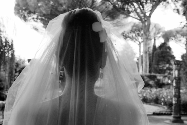 beautiful black and white photo taken from behind a bride with her hair in an up-do wearing a veil facing a garden - photo by Italian wedding photographer JoAnne Dunn